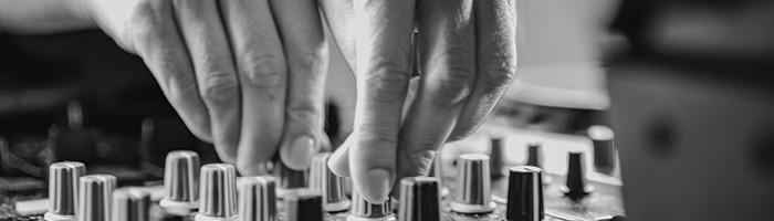Hands adjust the knobs on an audio mixing board.