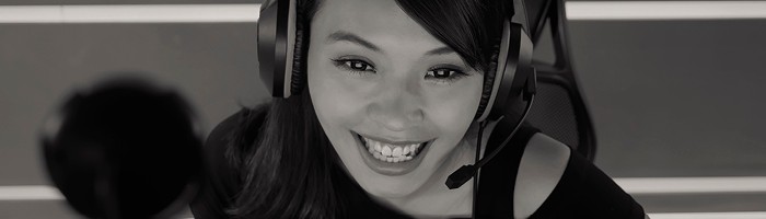 A woman of Asian descent smiles down and towards the viewer, as if gaming and laughing with friends on her headset.