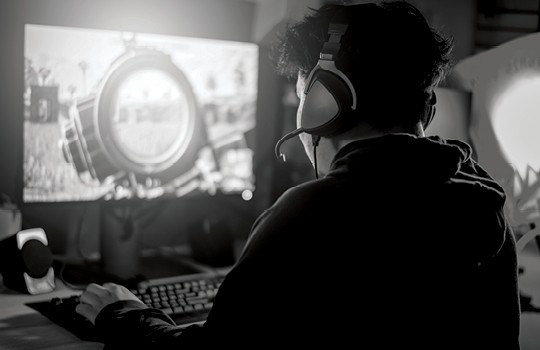 A gamer wearing a headset sits in front of a screen.